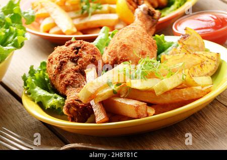 Gebratene Hühnerkeulen mit Pommes Frites auf dem Tisch Stockfoto