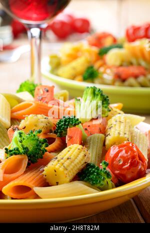 Pasta Penne mit Brokkoli, Karotten, Mais, serviert mit Rotwein Stockfoto