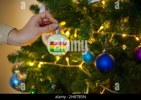 Ein Mädchen hält eine Dekoration auf einem Weihnachtsbaum mit der Flagge Boliviens Stockfoto