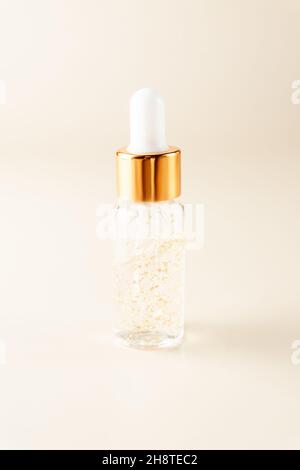 Transparente Flasche mit Beauty-Serum, Hyaluronsäure, 24k Gold und Vitaminen auf beigem Hintergrund. Luxuriöses Konzept für Gesicht- und Körperpflege zu Hause Stockfoto