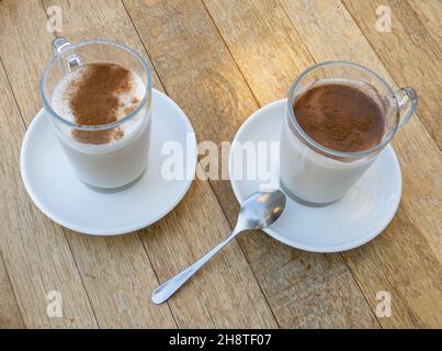 Grado, Italien - 6. Juli 2021: Zwei Tassen Kaffee mit Milch, mit Glaspüchern und Teller und einem Löffel Stockfoto