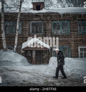 23rd. Februar 2019, Russland, Tomsk, älterer Mann geht am alten Holzgebäude vorbei Stockfoto