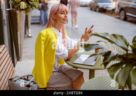 Junge Frau mit Smartphone und Laptop im Café im Freien Stockfoto