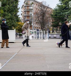 Drei ältere Menschen, die mit einer Corona-Schutzmaske auf einem Bürgersteig gehen. Eine Frau, die mit ihrem Hund läuft. Stockfoto