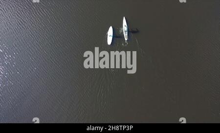 Luftaufnahme von nicht identifizierbaren Personen in Jacken, die an sonnigen Tagen auf einem SUP-Board auf einem ruhigen Fluss trainieren. Konzept des Wassertourismus, gesunde Lebensweise und Stockfoto