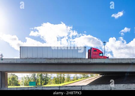 Industrial leistungsstarke rote Big Rig klassischen Sattelschlepper transportieren gewerbliche Fracht in trockenen van Sattelanhänger läuft auf der Betonbrücke über die wid Stockfoto