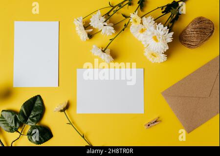 Leere Karte mit Umschlag und Blume ist auf gelbem Hintergrund platziert Stockfoto