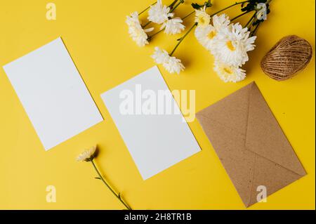 Leere Karte mit Umschlag und Blume ist auf gelbem Hintergrund platziert Stockfoto