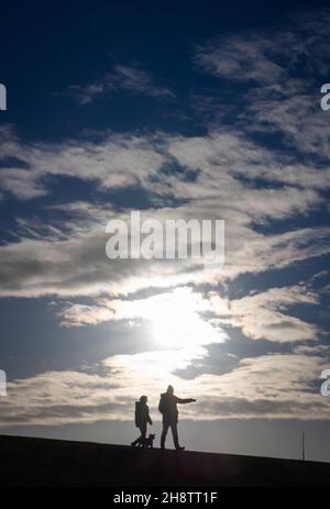 02. Dezember 2021, Schleswig-Holstein, Büsum: Zwei Menschen laufen auf dem Deich am Hafen von Büsum bei strahlendem Sonnenschein. Foto: Christian Charisius/dpa Stockfoto