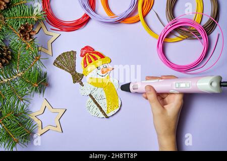 Ein Mädchen zeichnet einen Schneemann mit einem 3d-Stift auf einem violetten Hintergrund Stockfoto