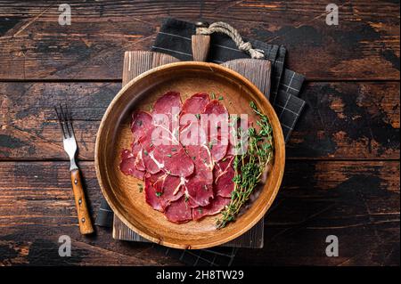 Pastrami-Scheiben, getrocknetes Rinderfleisch mit Kräutern in Holzplatte. Holzhintergrund. Draufsicht Stockfoto
