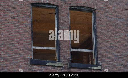 Zwei Fenster mit verwitterten schwarzen Rahmen auf einem alten Backsteingebäude Stockfoto