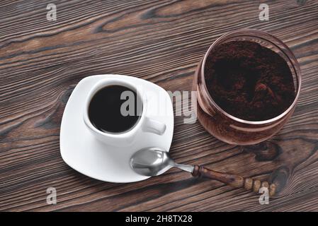 Kaffee in einer Tasse auf einem Steinständer gemahlener Kaffee in einem Glasgefäß Vintage-Kaffeelöffel, natürlicher Hintergrund aus Holz, selektiver Fokus, Nahaufnahme Stockfoto