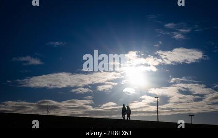 02. Dezember 2021, Schleswig-Holstein, Büsum: Zwei Menschen laufen auf dem Deich am Hafen von Büsum bei strahlendem Sonnenschein. Foto: Christian Charisius/dpa Stockfoto