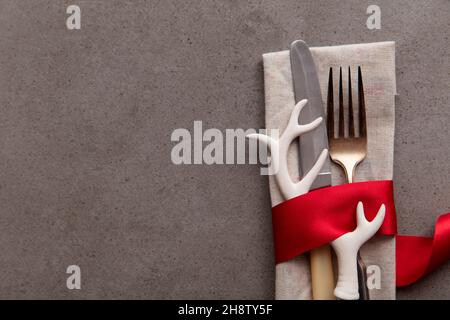 Festliche weihnachtliche Tischdekoration mit in ein rotes Band gewickeltem Besteck und Geweih-Dekoration Stockfoto
