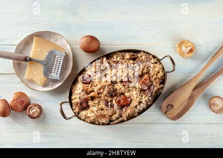 Pilzrisotto, rustikaler italienischer Reis mit Pilzen und Käse, mit Zutaten, Top Shot auf einem hölzernen Hintergrund Stockfoto