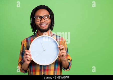 Foto von charmanten verträumt dunkle Haut Kerl gekleidet Hemd Brille halten Uhr suchen leeren Raum isoliert grüne Farbe Hintergrund Stockfoto