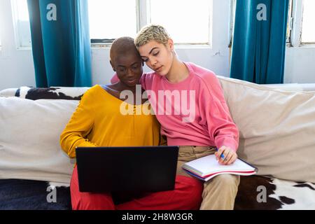 Lächelnde Frauen mit Laptop, während sie zu Hause auf dem Sofa sitzen Stockfoto