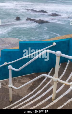 An einem kalten, windigen Tag im November führen Treppen hinunter zum Bude Sea Pool am Summerleaze Beach, Bude, North Cornwall, Großbritannien - ein Teil des künstlichen Gezeitenpools Stockfoto