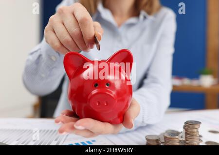 Geschäftsfrau wirft Münzen in Sparschwein am Tisch mit Grafiken aus der Nähe Stockfoto