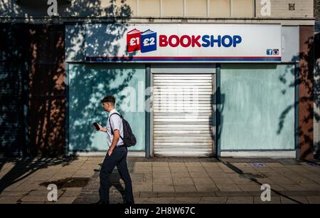 Mann mit seinem Handy, der an einem geschlossenen Buchladen in Rotherham vorbeiging Stockfoto