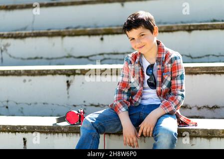 Fröhlicher Junge, der auf der Tribüne im Stadtpark sitzt, während er die Kamera anschaut Stockfoto