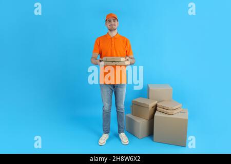 Lieferer hält Pizza auf blauem Hintergrund mit Schachteln Stockfoto