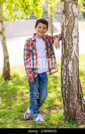 Fröhliches Jungen-Portrait, das im Stadtpark steht und dabei die Kamera anschaut Stockfoto