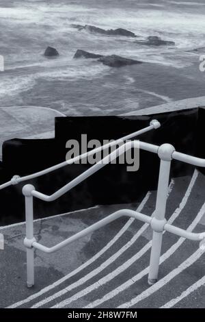 An einem kalten, windigen Tag im November führen Treppen hinunter zum Bude Sea Pool am Summerleaze Beach, Bude, North Cornwall, Großbritannien - ein Teil des künstlichen Gezeitenpools Stockfoto