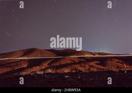 Nachtansicht von Pflanzen und Hügeln in der Wüste mit Licht- und Sternspuren und Nordstern am Rahmen im iran Stockfoto