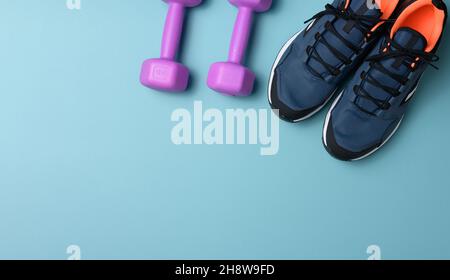 Paar blaue Sneaker und lila Kurzhanteln auf blauem Hintergrund, Sport. Speicherplatz kopieren Stockfoto