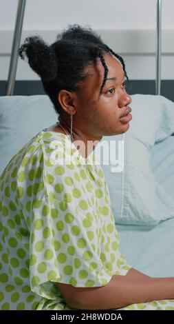 Porträt eines afroamerikanischen Patienten, der im Krankenhausbett sitzt und auf den Arzt wartet, um medizinische Unterstützung und Behandlung zur Heilung von Krankheiten zu geben. Junge Frau mit Infusionsbeutel fühlt sich krank Stockfoto