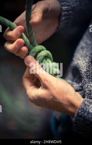 Detail mit den Händen eines Kletterers, der eine Acht an das Geschirr bindet. Stockfoto