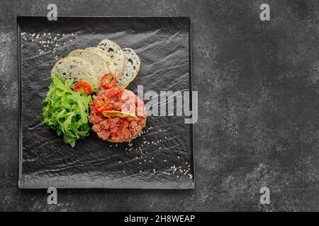 Lachs-Tartar mit Avocado auf schwarzem Teller Stockfoto