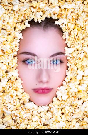 Das Gesicht im Popcorn. Porträt eines jungen schönen Mädchens auf einem Hintergrund aus goldenem Popcorn Stockfoto