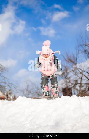 Winterlandschaft mit blauem Himmel. Kind in warmen Winteranzug hat Spaß, spielen und Angeln in der Schneeverwehung, Reiten Schneerutsche während des Spaziergangs in der Natur auf Stockfoto