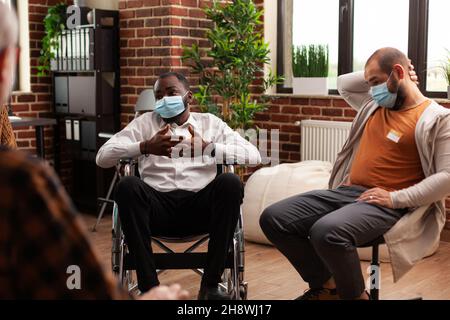 afroamerikanischer Mann mit Behinderung nimmt an einem Treffen mit Menschen Teil und erhält Beratung gegen Alkoholabhängigkeit während einer Coronavirus-Pandemie. Patienten, die bei der unterstützenden Gruppentherapie sprechen Stockfoto