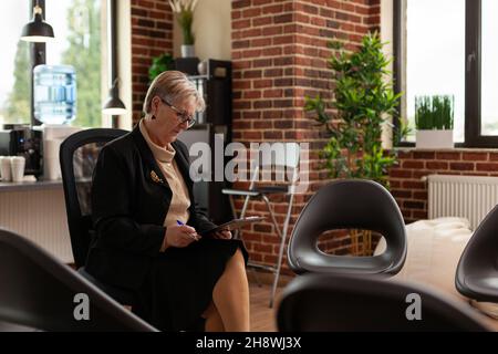 Psychiater mit Zwischenablage wartet auf eine Gruppe, die Leute trifft, im Kreis mit Stühlen sitzend. Frau Therapeutin Vorbereitung für Gruppentherapie Sitzung mit Menschen im Rehabilitationsbüro. Stockfoto