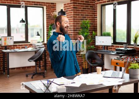Gelächlicher Geschäftsmann, der im Startup-Büro tanzt und ein erfolgreiches Marketing-Projekt bei der Geschäftspartnerschaft feiert. Erfolgreicher Vertrag durch den Executive Manager. Geschäftskonzept Stockfoto