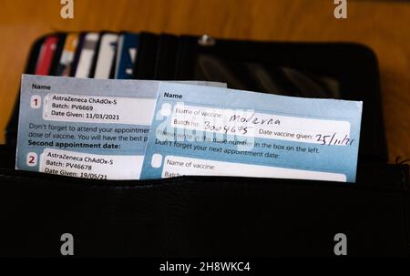 Covid-Impfpass in einem Geldbeutel. Ein Pass gilt für zwei Impfungen von AstraZeneca und der andere für einen Moderna-Auffrischungsimpfstoff. Stockfoto