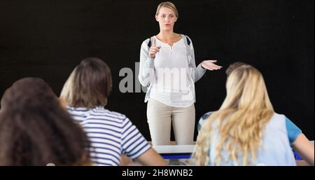 Lehrer gestikulierte, während er Erwachsene männliche und weibliche Schüler vor schwarzem Hintergrund erklärte Stockfoto