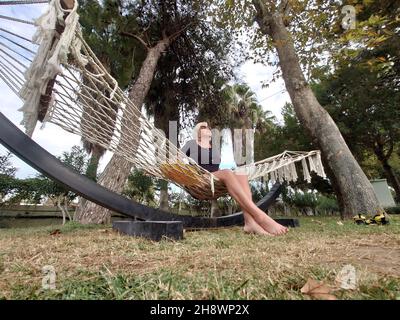 Barfuß unbeschwerte Frau, die sich auf einer Hängematte erholte und die Sommersonne mit ihrem Gesicht genoss, drehte das Sonnenlicht in einem niedrigen Winkel in einem Garten eines A auf Stockfoto