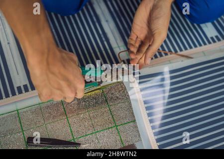 Master installiert einen warmen Fußboden im Raum. Installation der Fußbodenheizung Stockfoto