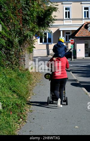 Stainz, Österreich - 23. September 2021: Unbekannte Mutter mit Kinderwagen und Huckepack, eine weitere lustige Art von Transport Stockfoto