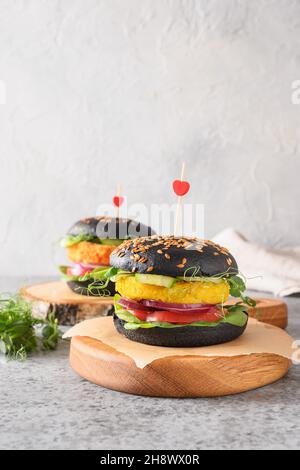 Veganer Burger auf pflanzlicher Basis mit Gemüsefleischbällchen und schwarzen Kohlebuns auf grauem Hintergrund, mit Liebe hergestellt. Nahaufnahme. Vertikal. Gesunde Lebensmittel und din Stockfoto