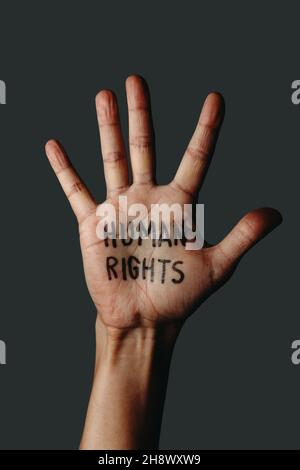 Nahaufnahme der offenen Hand eines Mannes mit dem Text Menschenrechte in seiner Handfläche, auf einem dunkelgrauen Hintergrund Stockfoto