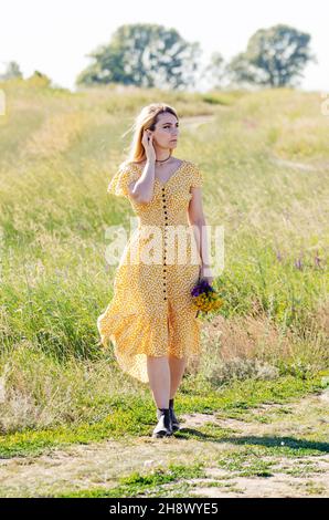 Junge blonde kaukasische weibliche Modell mit Blumen in ihrer Hand Spaziergang im Freien Sommer sonnigen Tag. Stockfoto