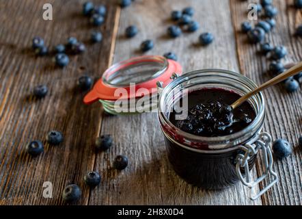 Hausgemachte Heidelbeermarmelade im Glas mit Löffel isoliert auf Holztisch mit Kopierplatz Stockfoto