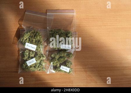 Getrocknete Cannabisknospen in Plastiktüten auf einem Holztisch. Brauner Hintergrund. Sortenreine Marihuanablüten. Draufsicht, flach liegend. Tägliche Hanfroutine. Stockfoto