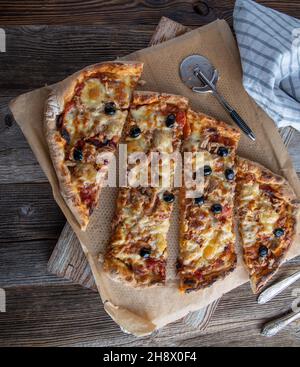 Hausgemachte Pizza mit Thunfisch, Zwiebeln, Käse und Tomatensauce. In Stücken auf Holztisch mit Pizzaschneider serviert Stockfoto